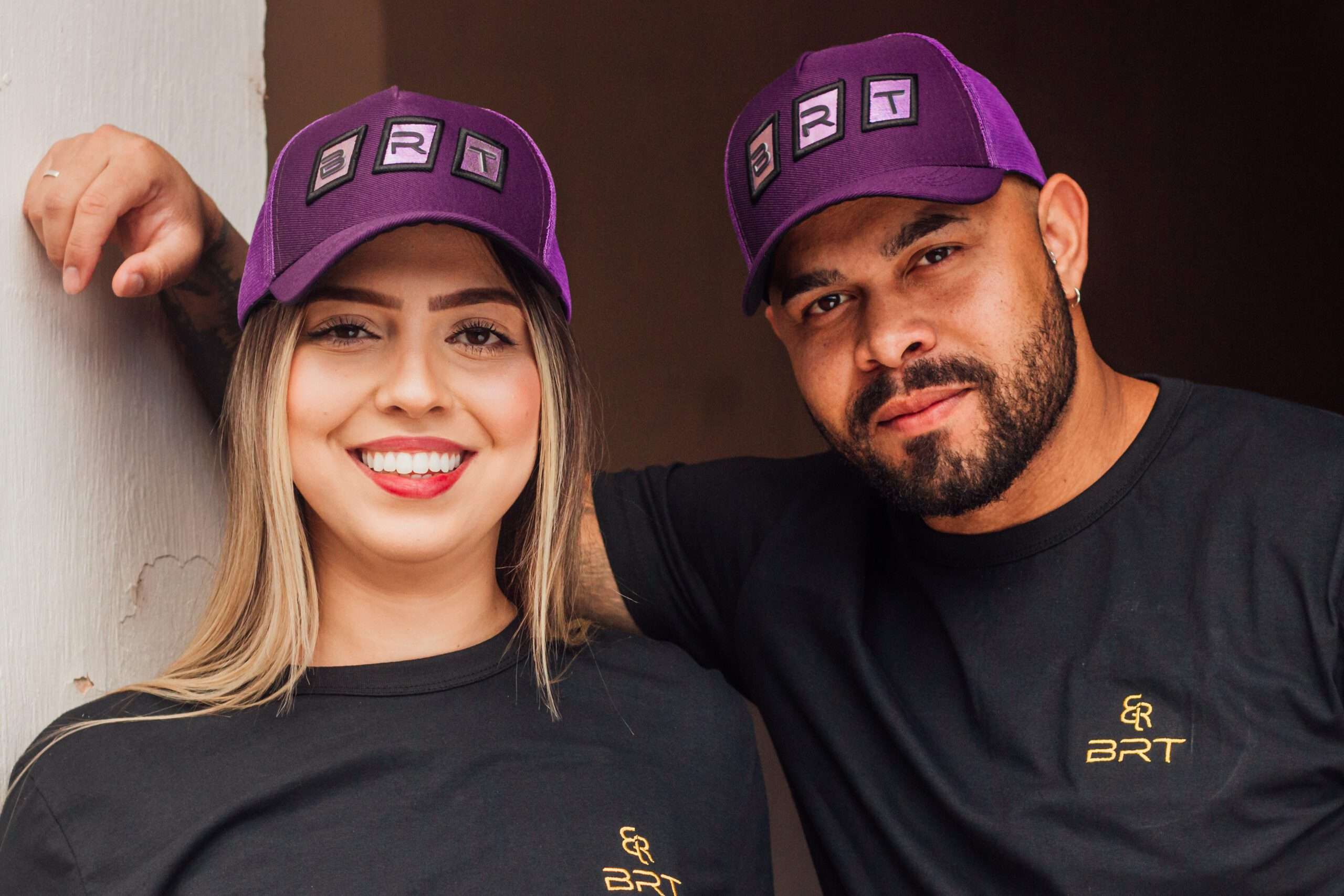 Pessoas sorrindo olhando para a câmera, usando uma camiseta e os bonés da BRT