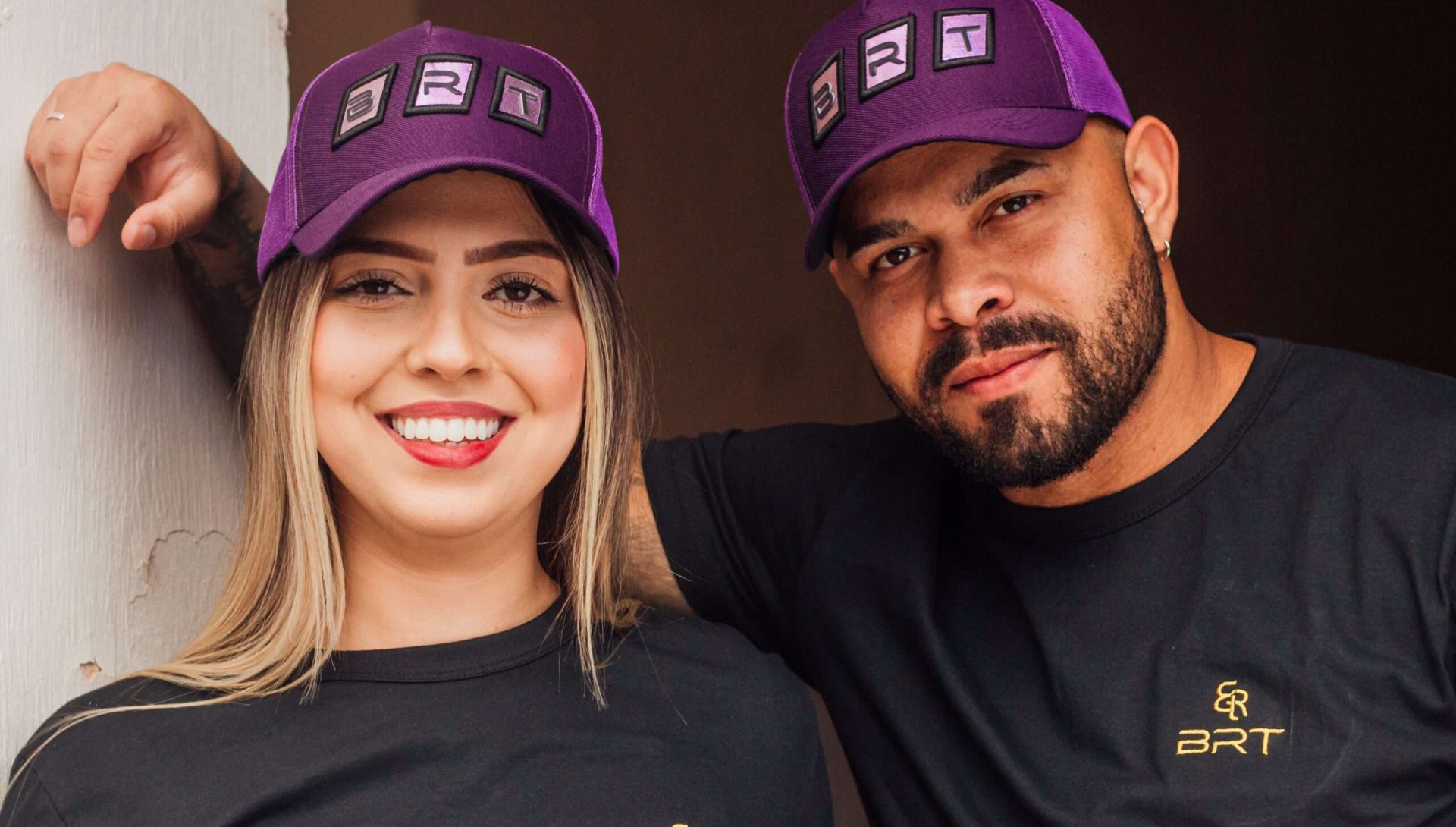 Pessoas sorrindo olhando para a câmera, usando uma camiseta e os bonés da BRT